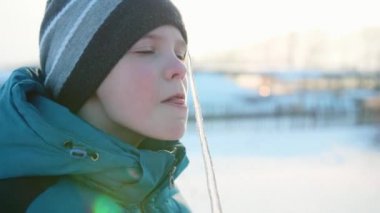 Bir saçağı yalama bir çocuk. Karlı soğuk güneşli gün. Eğlence ve oyun temiz havada.