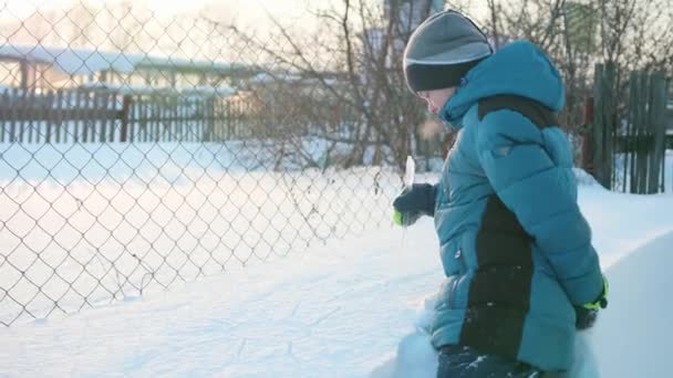 Een tiener in een winter Park schildert een ijspegel in de sneeuw. Besneeuwde frosty zonnige dag. Pret en spelen in de frisse lucht. — Stockvideo