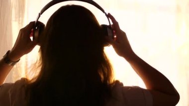 Genç bir kız pencereye gelir ve müzik dinlemek için kulaklık elbiseler. Gün batımı, kadının Kulaklığımda melodi ile arka plan bulanık.