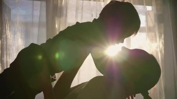 Modern som håller ett litet barn på händerna. Solens strålar genom fönstret. Den skratt och glädje av barnet. — Stockvideo