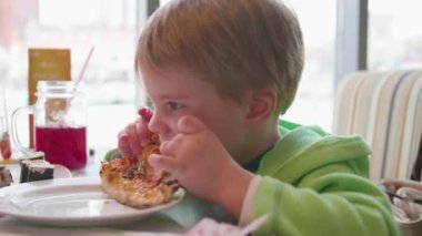 Küçük bir çocuk bir fast food Cafe pizza yiyor. Pizza peyniri, jambon, domates ve beyaz zemin üzerine tabak içinde otlar ile.