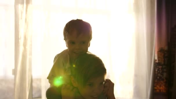 Dos niños jugando en la habitación. El hermano mayor sostiene al bebé sobre sus hombros, los muchachos ríen y sonríen — Vídeos de Stock