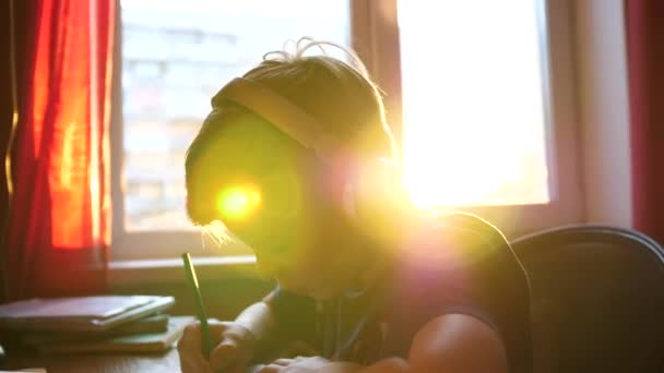 De student aan een bureau zit en doet zijn werk. Onderwijs op school. De zonnestralen door het glas. — Stockvideo