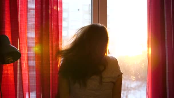 창에서 이른 아침 서에서 소녀 커튼을 엽니다. 태양 광선은 유리를 통해 통과 하 고 아침 빛을 가진 룸을 밝게. — 비디오