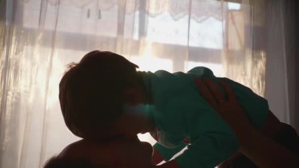 Madre sosteniendo a un niño pequeño en sus manos. Rayos de sol a través de la ventana. La risa y la alegría del bebé . — Vídeo de stock