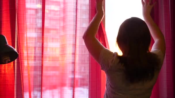 행복 한 젊은 여자는 창에 커튼을 엽니다. 태양 광선 조명 룸과 여자 창을 통해 전달 합니다. 일몰 시간 — 비디오