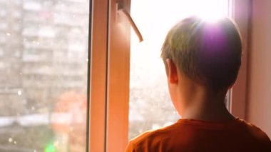 Güneşli kış günü. Genç bir adam ve pencerenin yanındaki standları düşen kar görünüyor