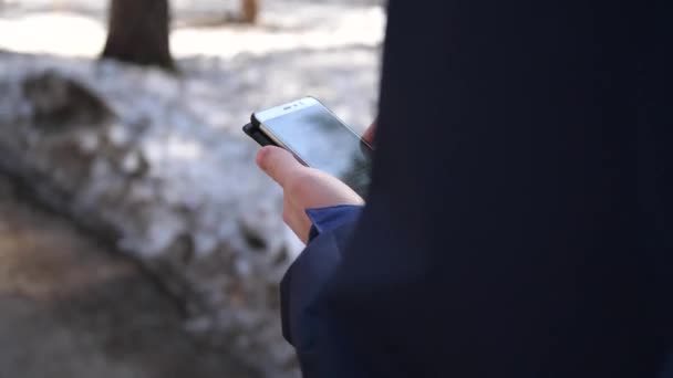 En ung kille går nerför gatan och använder telefonen för internet. Närbild. — Stockvideo