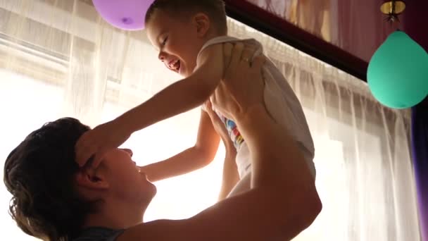Jovem pai brincando com o bebê, segurando-o nos meus braços, jogue para cima. Raios solares pela janela. Risos e alegria da criança . — Vídeo de Stock