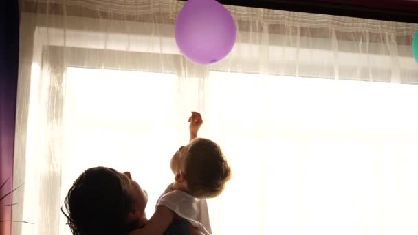 Joven padre sosteniendo a su pequeño hijo cerca de una ventana. Rayos de sol a través de la ventana. La risa y la alegría del niño . — Vídeos de Stock