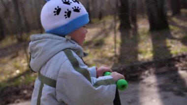 Çocuk erken ilkbaharda bir scooter park gezintisi. Eriyen kar, kar ve su birikintileri asfalt üzerinde. Doğa sporları
