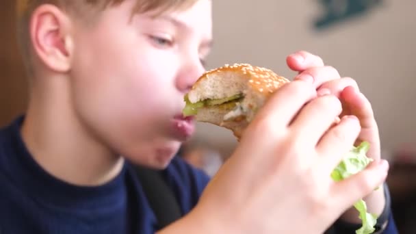 Een kind eet een broodje met een kotelet en kaas in een fast food restaurant — Stockvideo