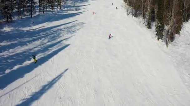 Skidbacke. Skidåkare och snowboardåkare rullar nerför banan. Flygfoto av en skidåkare nedför en bred skidbacke — Stockvideo