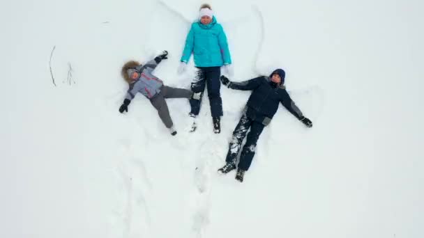 Çocuklu bir aile ormandaki bir açıklıkta kar meleği figürü yapar. Karda yatan bir kız ve çocukların hava fotoğrafları.. — Stok video