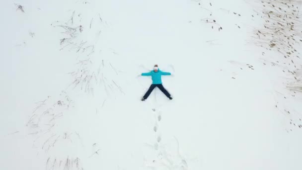 Bir kız ormandaki bir açıklıkta kar meleği figürü yapıyor. Karda yatan bir kızın havadan çekilmiş fotoğrafı.. — Stok video