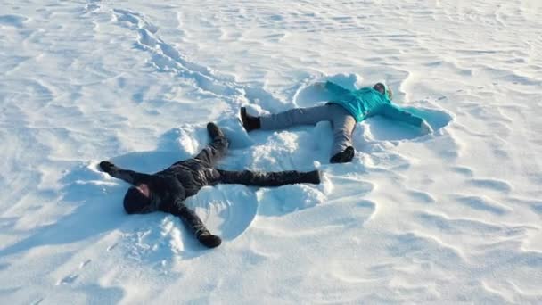 Uma família faz uma figura de um anjo da neve em uma clareira na floresta. Fotografia aérea de uma menina e um menino deitado na neve . — Vídeo de Stock