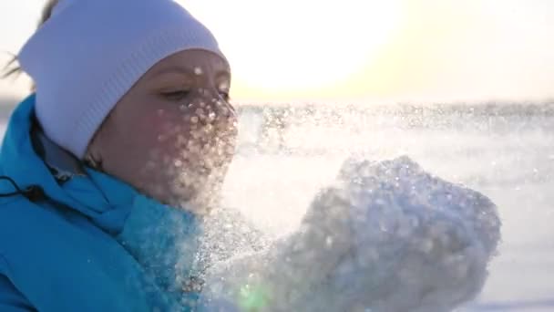 Meisje blaast sneeuw uit handen op zonnige achtergrond — Stockvideo