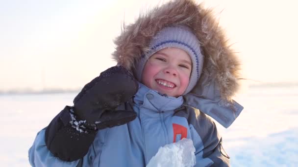Счастливый ребенок, весело смеющийся в зимнем парке в солнечный день. снежный зимний пейзаж. на открытом воздухе — стоковое видео