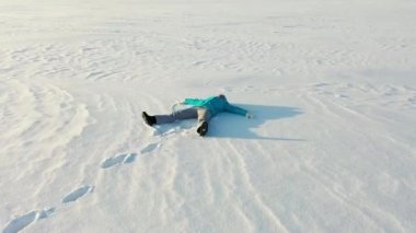 Bir kız ormandaki bir açıklıkta kar meleği figürü yapıyor. Karda yatan bir kızın havadan çekilmiş fotoğrafı..