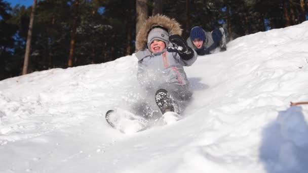 Los niños cabalgan en una montaña nevada. En cámara lenta. Paisaje invernal nevado. Deportes al aire libre — Vídeos de Stock