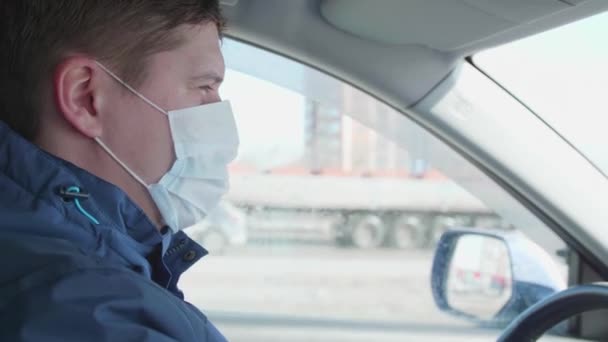 Guy fährt Auto. Die medizinische Maske auf dem Gesicht. Menschen nutzen zusätzlichen Schutz vor Coronavirus. — Stockvideo