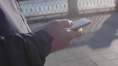 Genç bir adam sokakta yürüyor ve telefonu internet için kullanıyor. Yakın plan..