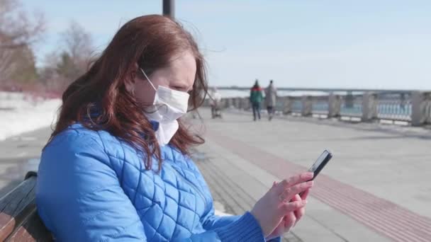 Seorang gadis dengan ponsel dengan topeng pelindung di jalan. Pencegahan dan perlindungan kesehatan dan keselamatan hidup. — Stok Video