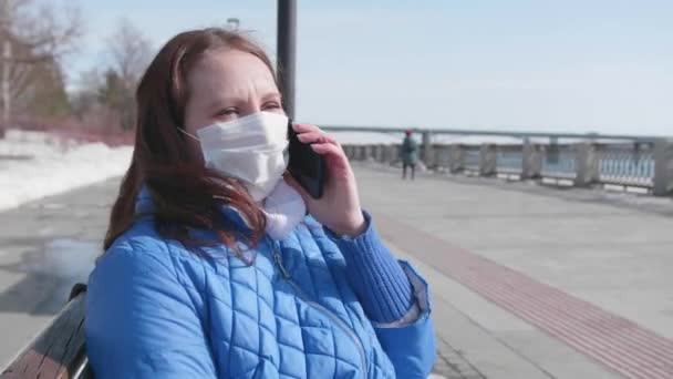 Une fille parle sur le téléphone portable avec un masque de protection dans la rue. Prévention et protection de la santé et de la vie . — Video