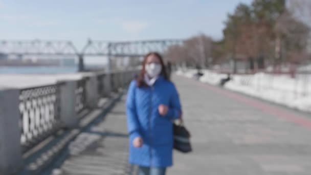 Дівчина гуляє в захисній масці на березі річки. Запобігання та захист здоров'я та безпеки життя . — стокове відео