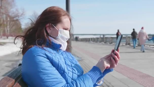 Una ragazza con il cellulare con una maschera protettiva per strada. Prevenzione e protezione della salute e della sicurezza della vita . — Video Stock