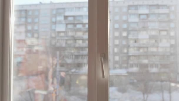 Un joven se para cerca de la ventana y se pone auriculares para escuchar música. Fondo borroso con puesta de sol, adolescente disfrutando de la música en los auriculares . — Vídeos de Stock