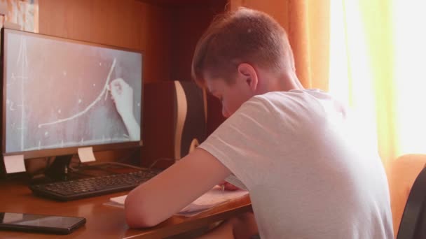 El estudiante observa la lección en línea y aprende en casa. Un joven hace su tarea mientras mira la pantalla de la computadora. Educación escolar . — Vídeos de Stock