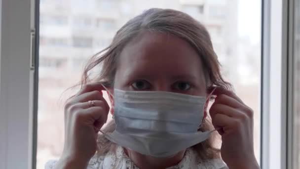 Een meisje met een beschermend masker staat bij een raam in het ziekenhuis. Preventie en bescherming van de gezondheid en de veiligheid van het leven. — Stockvideo