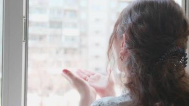 Koruyucu maskeli kız hastanedeymiş. Kız açık bir pencereden iletişim kuruyor, selamlar ve öpücükler gönderiyor. Sağlık ve can güvenliğinin önlenmesi ve korunması.