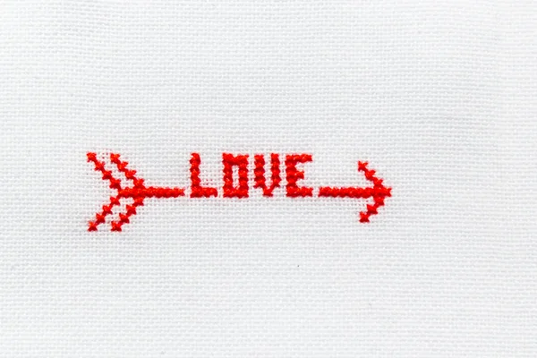 La flecha con la palabra amor bordado hilo rojo sobre tela blanca . — Foto de Stock