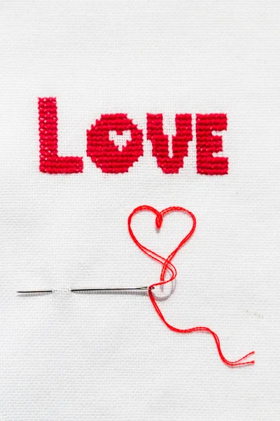 The word love embroidered red thread on white fabric.