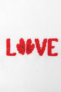 Kırmızı iplik beyaz kumaş üzerine işlenmiş kelime aşk.