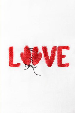 Kırmızı iplik beyaz kumaş üzerine işlenmiş kelime aşk.