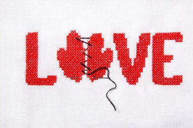 Kırmızı iplik beyaz kumaş üzerine işlenmiş kelime aşk.