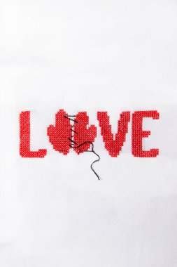 Kırmızı iplik beyaz kumaş üzerine işlenmiş kelime aşk.