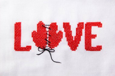 Kırmızı iplik beyaz kumaş üzerine işlenmiş kelime aşk.