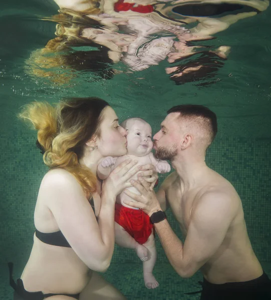 Happy family Mother and father kiss their little son underwater in the pool. Mom, Dad and little boy underwater in the pool.