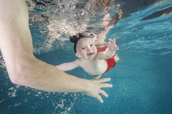 Little baby boy learning to swim underwater in a swimming pool, papa holding the child. Healthy family lifestyle and children water sports activity