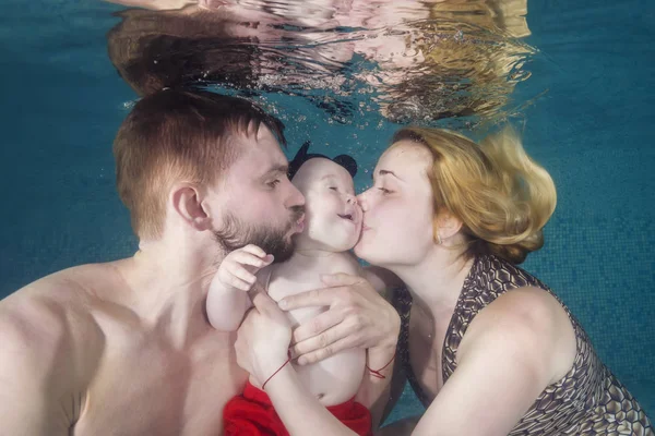 Dad and mom kiss a little boy underwater in the pool. Healthy family lifestyle and children water sports activity.