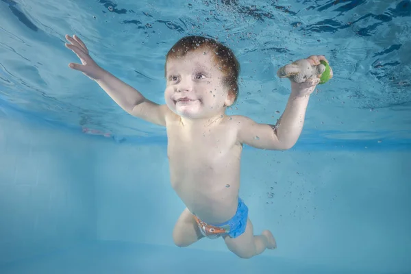 Funny baby boy with toy plays underwater in the pool. Healthy family lifestyle and children water sports activity. Child development, disease prevention