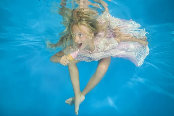 Girl in white dress eating ice cream underwater. Young beautiful girl poses underwater in the pool.