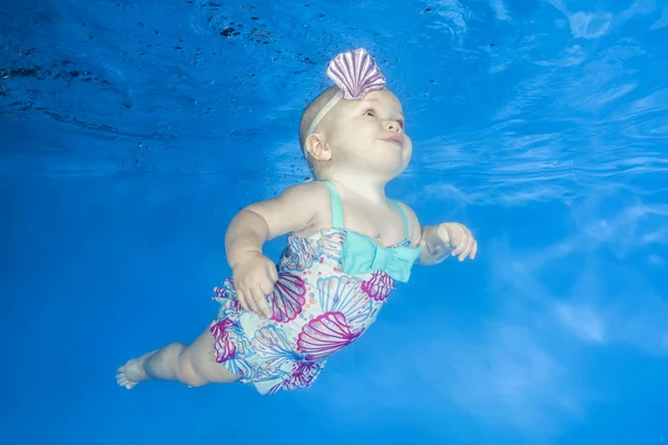 Little girl learns to swims underwater. Baby swimming underwater in the pool on a blue water background. Healthy family lifestyle and children water sports activity.