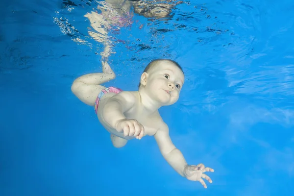 Little girl learns to swims underwater. Baby swimming underwater in the pool on a blue water background. Healthy family lifestyle and children water sports activity.