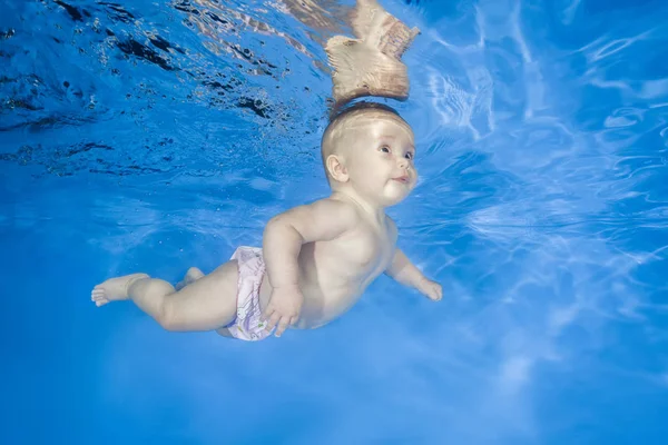 Little baby learns to swims underwater. Baby swimming underwater in the pool on a blue water background. Healthy family lifestyle and children water sports activity.