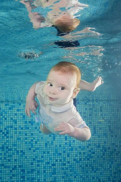 Funny face portrait of baby boy swimming and diving underwater with fun in the pool. Healthy family lifestyle and children water sports activity.